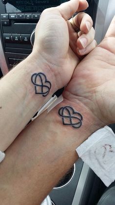 two people with matching tattoos on their wrists holding each other's hands in the car