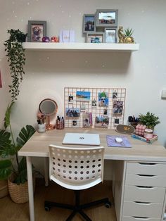 a white desk topped with a laptop computer next to a potted plant and framed pictures