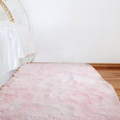 a white bed sitting next to a pink rug on top of a hard wood floor