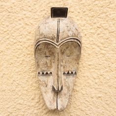 an old mask is mounted on the side of a stucco - colored wall with black accents