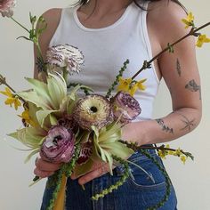 a woman holding a bouquet of flowers in her hands and wearing a white tank top