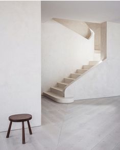 an empty room with stairs and a stool in the foreground, against a white wall