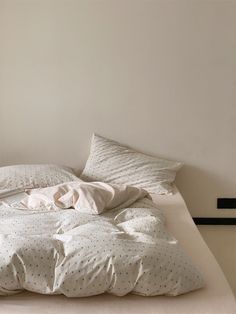 an unmade bed with white sheets and polka dot pillows on it in a bedroom