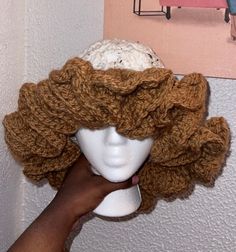 a person is holding up a crocheted hat on a mannequin head