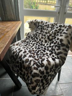 a leopard print chair sitting in front of a window next to a wooden table with a glass door