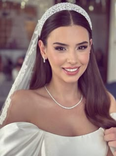 a woman wearing a bridal gown and tiara smiling at the camera with her hand on her shoulder