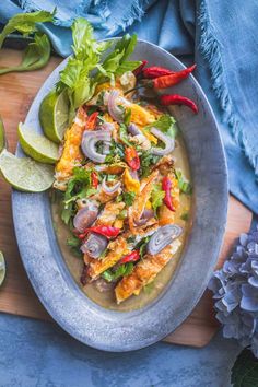 a plate full of food on a wooden cutting board next to some limes and blue flowers