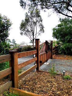 a wooden fence with gravel and trees in the background