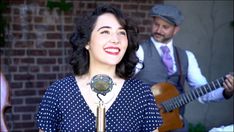 a woman singing into a microphone next to a man with a guitar and an instrument