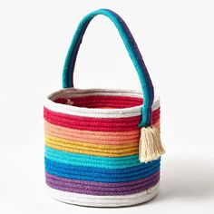 a multicolored woven basket with tassels on the handles and bottom, sitting against a white background