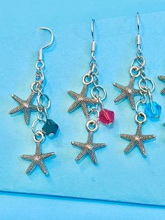 three starfish charms are hanging from silver earwires on a light blue background