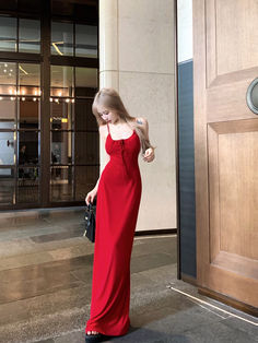 a woman in a long red dress is standing by a door and looking down at her purse