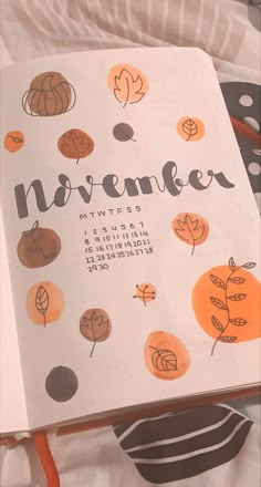 an open notebook with the word november written in black and orange on it, surrounded by fall leaves