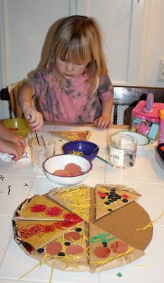 two children are sitting at a table making pizza slices out of paper plates and bowls