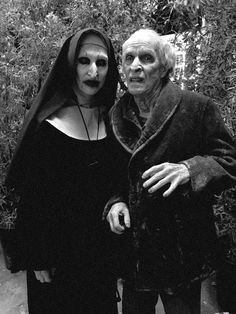 an old man and woman dressed up as nun and nun in front of some bushes