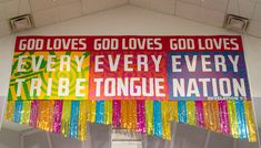 there is a large banner hanging from the ceiling in front of a window that says god loves god loves every tribe tongue nation