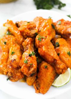 a white plate topped with chicken wings covered in sauce and garnished with parsley