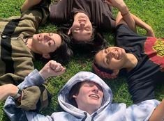 four people laying on the grass with their hands in the air and one person wearing a hoodie