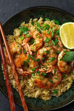 shrimp and rice dish with chopsticks on black plate next to lemon slice, garnished with parsley