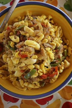 a yellow bowl filled with pasta and vegetables on top of a colorful table cloth next to a fork