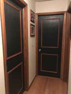 an empty hallway with two doors and pictures on the wall above them, along with hardwood flooring