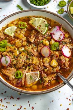 a bowl filled with meat and vegetables on top of a white table next to limes