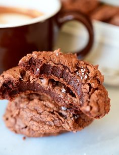 two chocolate cookies sitting next to each other on a white plate with a cup of coffee in the background