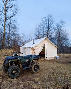 an atv parked next to a tent in the middle of a field with trees and grass