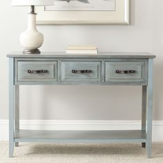 a blue table with two drawers and a lamp on it in front of a white wall