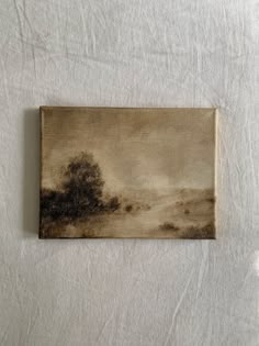 a painting is shown on a white sheet with a tree in the distance and clouds above it