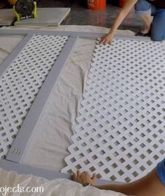 two people laying on the ground working on a piece of plastic sheet with holes in it