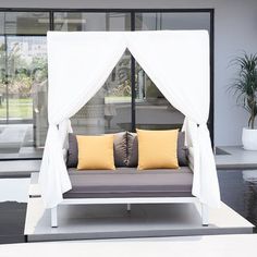 a white canopy bed with yellow and gray pillows in front of a large glass window