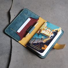 a notebook and pen sitting on the ground next to an open passport case with a notepad in it