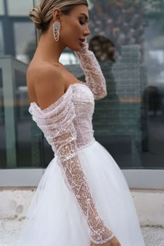 a woman in a white wedding dress with long sleeves and lace on her arms is looking away from the camera