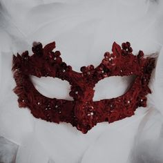 a red masquerade on white fabric with feathers in the foreground and an eye patch at the top