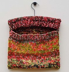 a multicolored sweater hanging from a hook on a white wall with an object attached to it