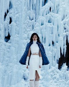 a woman standing in front of an ice waterfall wearing white clothes and knee high boots