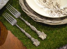 there are two forks on the grass next to some plates and silver utensils