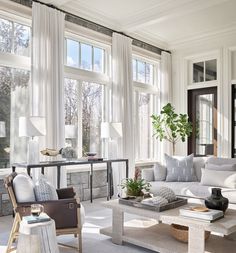 a living room filled with furniture and lots of windows covered in white curtained curtains