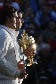 a tennis player holding a trophy in front of his face with spectators watching from the stands