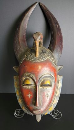 an old mask with horns on it is sitting on a table next to a gray wall