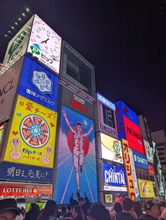 a crowd of people standing in front of a tall building with many advertisements on it