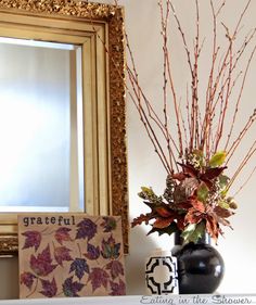 a vase filled with flowers sitting next to a mirror on top of a mantle covered in leaves