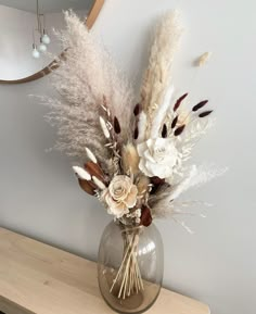 a vase filled with white flowers and feathers on top of a wooden table next to a mirror