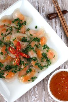 a white plate topped with dumplings covered in veggies next to dipping sauce