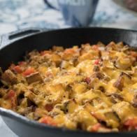 a skillet filled with cheese and meat on top of a counter next to a cup