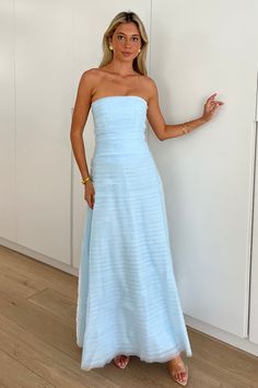 a woman in a blue strapless dress leaning against a wall with her hand on the side