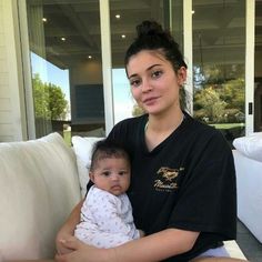 a woman sitting on a couch holding a baby in her arms and looking at the camera