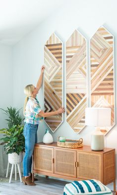 a woman standing next to a wooden table in front of a wall mounted art piece