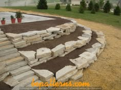 a stone wall in the middle of a field with potted plants and dirt around it